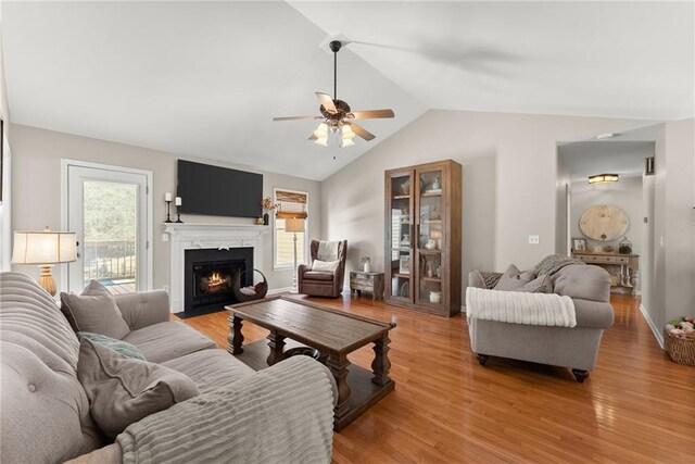 living room featuring light wood-type flooring, a fireplace with flush hearth, and ceiling fan