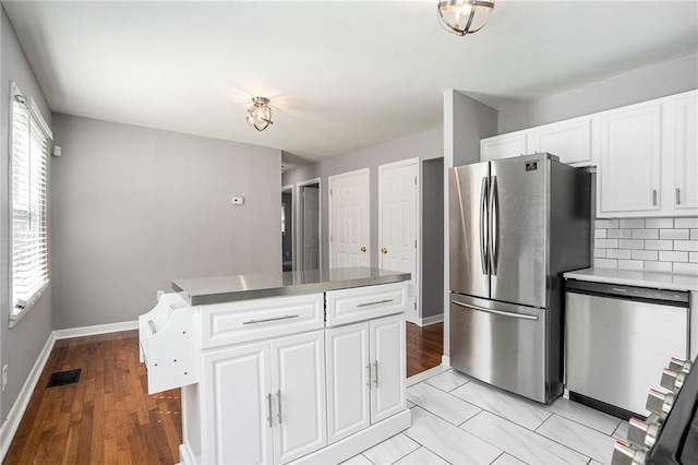 kitchen with white cabinets, appliances with stainless steel finishes, light hardwood / wood-style floors, and tasteful backsplash