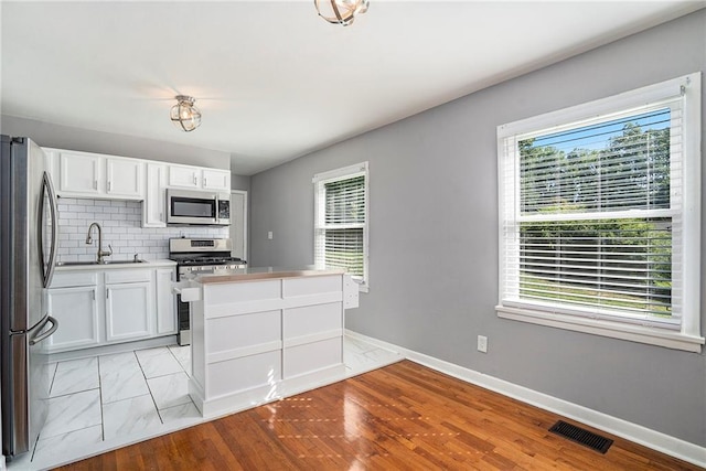 kitchen featuring backsplash, white cabinets, sink, light wood-type flooring, and appliances with stainless steel finishes