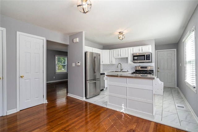 kitchen featuring sink, stainless steel appliances, light hardwood / wood-style floors, decorative backsplash, and white cabinets