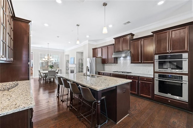 kitchen with an island with sink, stainless steel appliances, light stone countertops, and decorative light fixtures