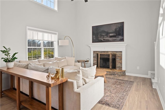 living room featuring ceiling fan, a fireplace, a high ceiling, and light hardwood / wood-style flooring