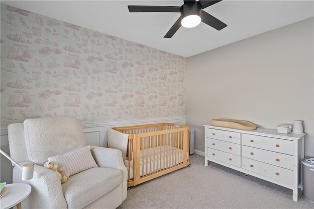 carpeted bedroom featuring ceiling fan and a crib