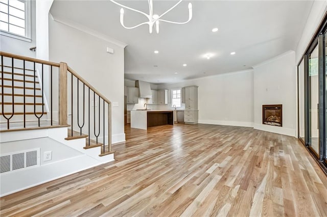 unfurnished living room with ornamental molding, a notable chandelier, and light hardwood / wood-style flooring