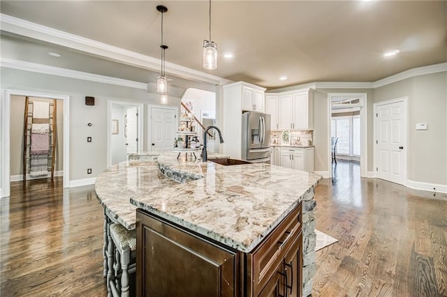 kitchen with hanging light fixtures, dark hardwood / wood-style flooring, sink, stainless steel fridge with ice dispenser, and a center island with sink