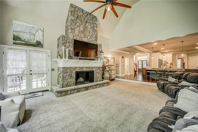 carpeted living room featuring ceiling fan, a stone fireplace, a high ceiling, and french doors