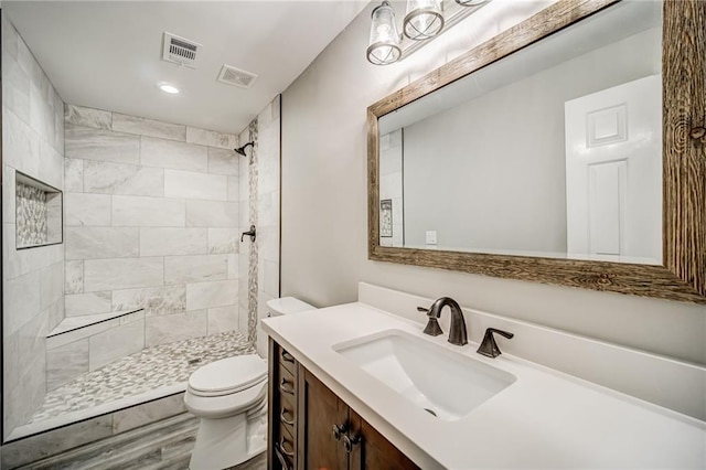 bathroom with toilet, a tile shower, vanity, and hardwood / wood-style flooring