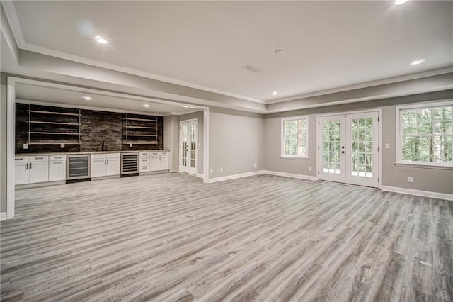 unfurnished living room featuring french doors, light hardwood / wood-style floors, sink, and wine cooler