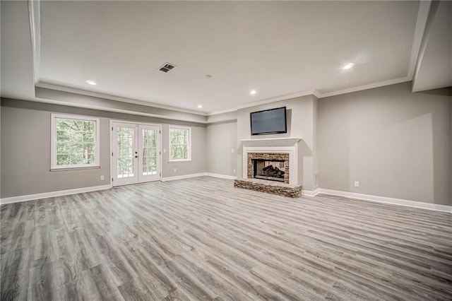 unfurnished living room featuring french doors, ornamental molding, hardwood / wood-style flooring, and a stone fireplace