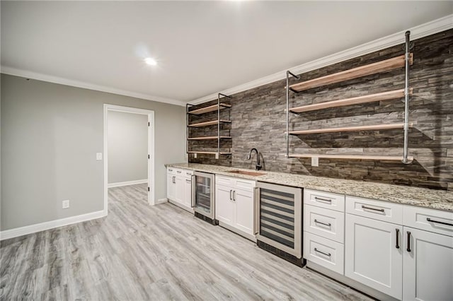 bar with light wood-type flooring, beverage cooler, white cabinetry, and sink