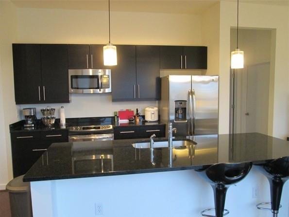 kitchen featuring decorative light fixtures, a sink, a kitchen breakfast bar, appliances with stainless steel finishes, and a center island with sink