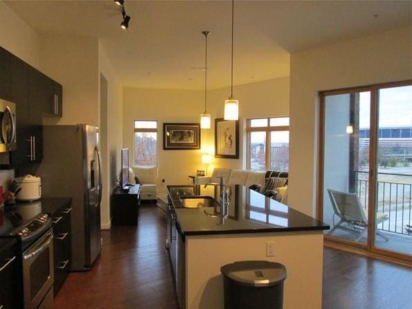 kitchen with a center island with sink, dark wood finished floors, dark countertops, stainless steel appliances, and a sink