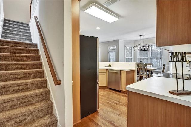 kitchen featuring light wood finished floors, an inviting chandelier, appliances with stainless steel finishes, light countertops, and hanging light fixtures