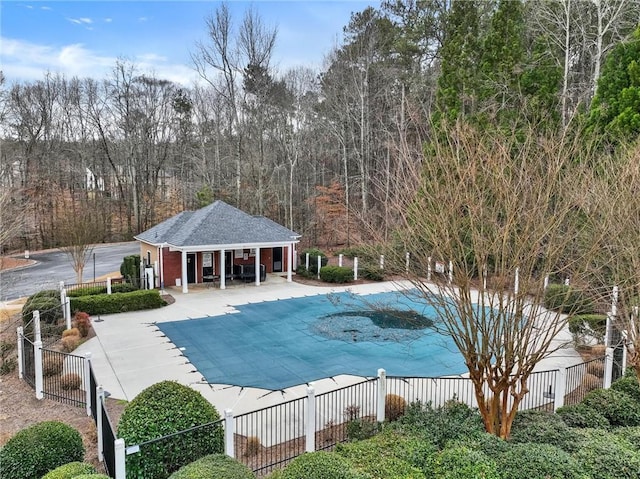 community pool with an exterior structure, a patio area, an outbuilding, and fence