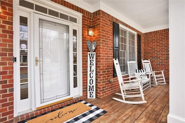 view of exterior entry featuring covered porch and brick siding