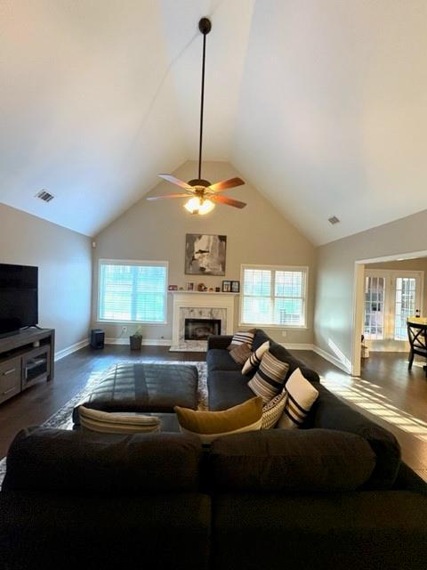 living room featuring high vaulted ceiling, wood finished floors, visible vents, a high end fireplace, and baseboards