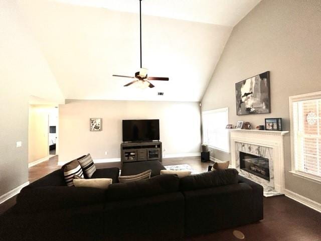 living area with high vaulted ceiling, a high end fireplace, baseboards, a ceiling fan, and dark wood-style floors