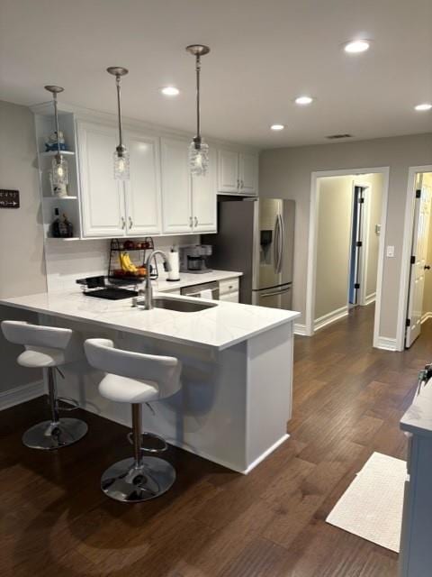 kitchen with stainless steel fridge, white cabinets, a breakfast bar area, a peninsula, and a sink