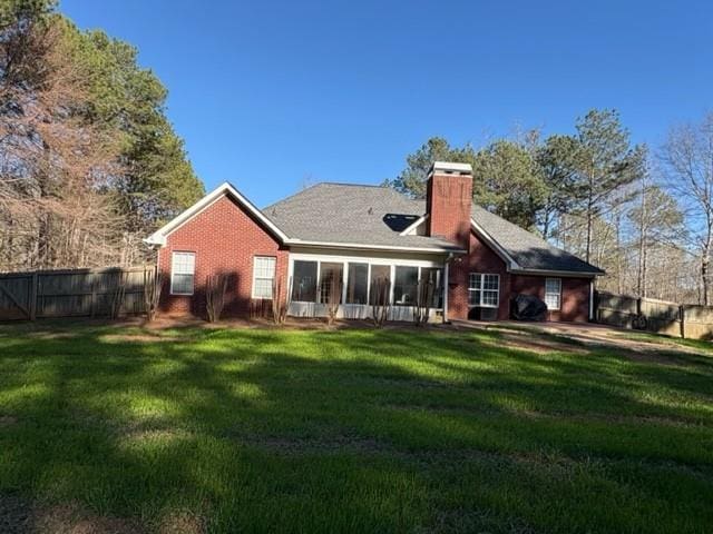 rear view of property featuring brick siding, fence, a sunroom, a yard, and a chimney