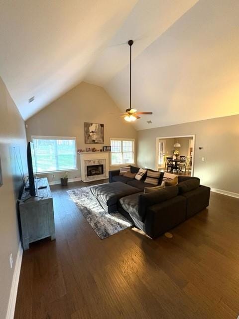 living area with dark wood finished floors, a fireplace with flush hearth, a ceiling fan, high vaulted ceiling, and baseboards