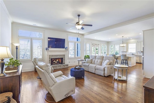 living area with baseboards, a stone fireplace, crown molding, and wood finished floors