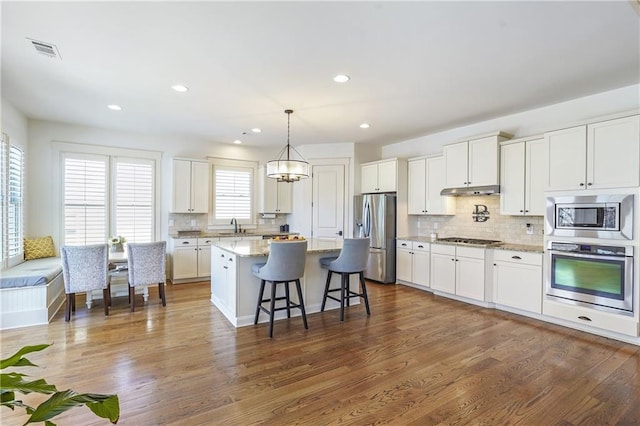 kitchen featuring light stone counters, a kitchen island, visible vents, white cabinets, and appliances with stainless steel finishes