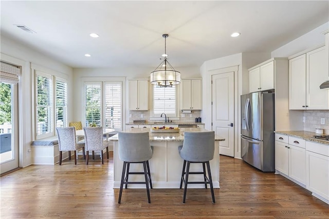 kitchen featuring hanging light fixtures, light stone counters, white cabinetry, and stainless steel fridge with ice dispenser