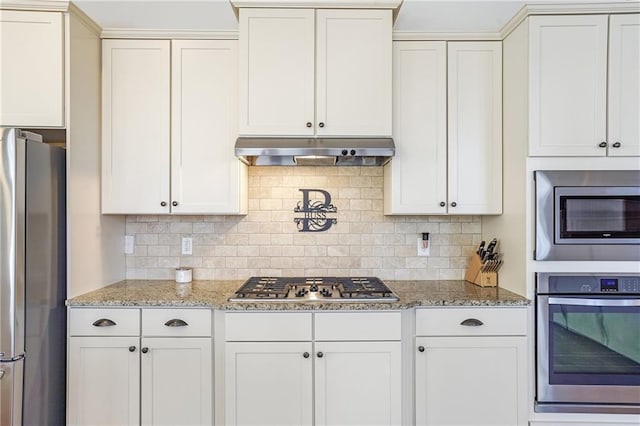 kitchen featuring light stone countertops, under cabinet range hood, white cabinetry, and appliances with stainless steel finishes