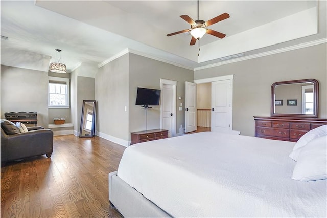 bedroom featuring a raised ceiling, ornamental molding, ceiling fan, wood finished floors, and baseboards