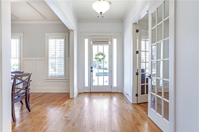 entrance foyer featuring light wood-style floors, ornamental molding, a decorative wall, and a wealth of natural light