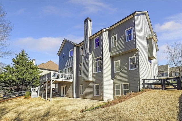 back of house featuring a chimney, fence, a deck, and a lawn