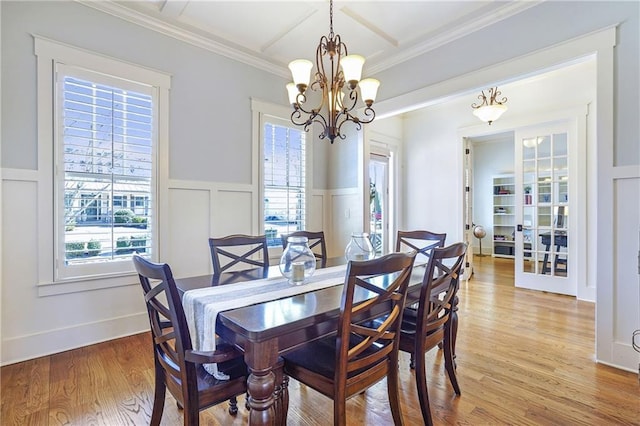 dining room featuring wainscoting, crown molding, light wood-type flooring, a decorative wall, and a notable chandelier