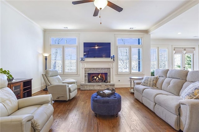 living area featuring baseboards, a stone fireplace, crown molding, and wood finished floors