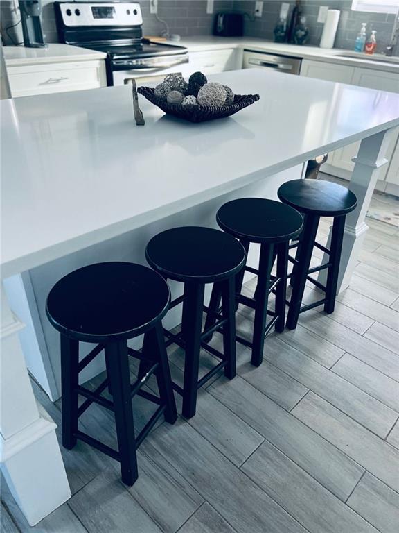 kitchen with light wood-type flooring, white electric range, a breakfast bar area, and white cabinets