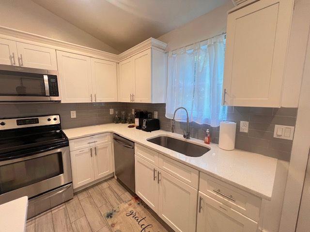 kitchen featuring appliances with stainless steel finishes, decorative backsplash, white cabinetry, vaulted ceiling, and sink