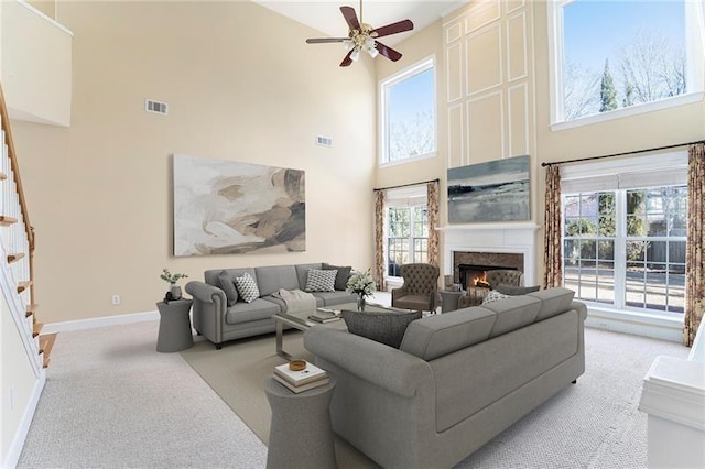 3505 Belridge Ln, Smyrna, GA 30080 - living room featuring a towering ceiling, a glass covered fireplace, stairs, a ceiling fan, and light carpet