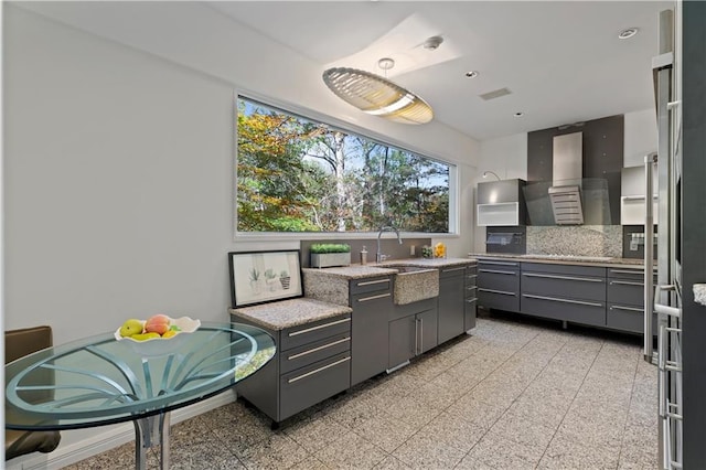 kitchen featuring wall chimney exhaust hood, gray cabinets, sink, and backsplash