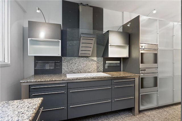 kitchen with gray cabinets, white electric cooktop, double oven, backsplash, and light stone countertops