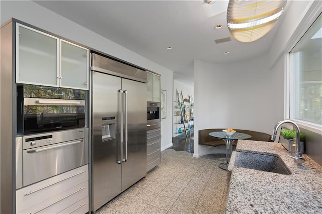 kitchen featuring stainless steel appliances, light stone countertops, sink, and backsplash