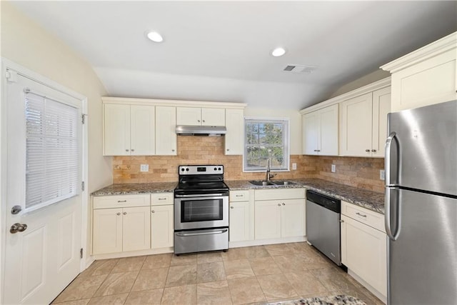 kitchen with lofted ceiling, sink, dark stone countertops, stainless steel appliances, and decorative backsplash