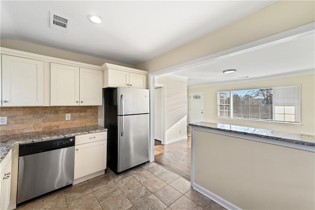 kitchen with tasteful backsplash, appliances with stainless steel finishes, white cabinets, and light stone counters