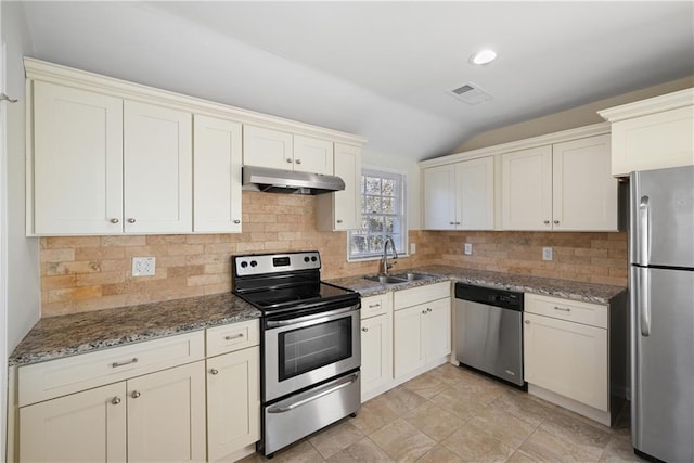 kitchen with sink, vaulted ceiling, dark stone countertops, stainless steel appliances, and backsplash