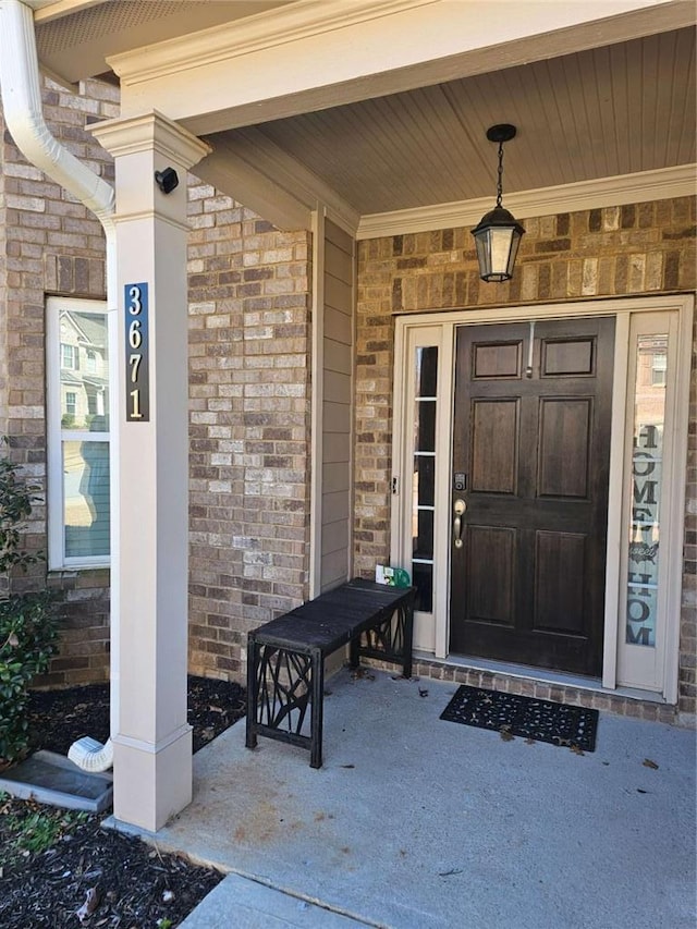 doorway to property featuring a porch and brick siding