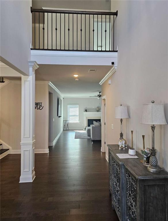 hall featuring ornamental molding, decorative columns, dark wood-style floors, and stairs