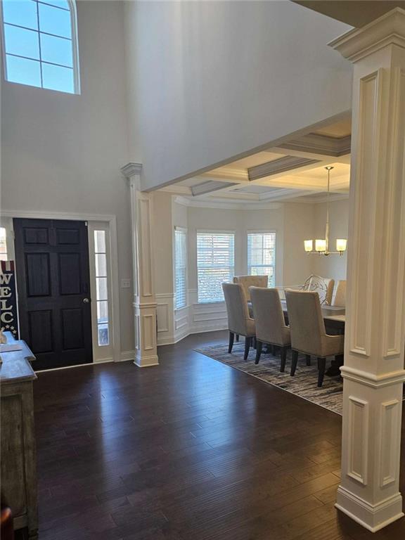 entrance foyer featuring a chandelier, a decorative wall, coffered ceiling, dark wood-style floors, and ornate columns