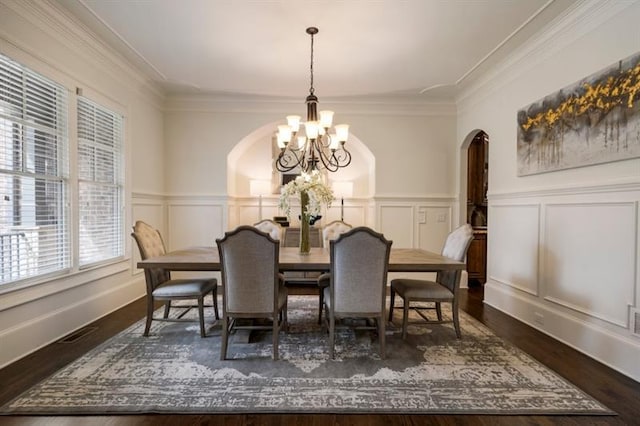 dining space with visible vents, arched walkways, wood finished floors, an inviting chandelier, and a decorative wall