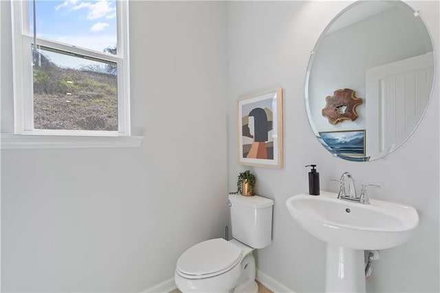 half bathroom with baseboards, a sink, and toilet