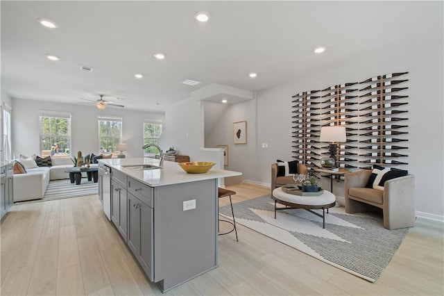 kitchen featuring gray cabinetry, a sink, a kitchen breakfast bar, open floor plan, and light wood-type flooring