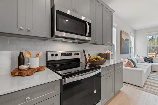 kitchen with light countertops, decorative backsplash, gray cabinetry, appliances with stainless steel finishes, and open floor plan