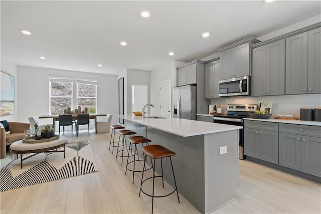 kitchen with appliances with stainless steel finishes, a kitchen breakfast bar, an island with sink, and gray cabinetry